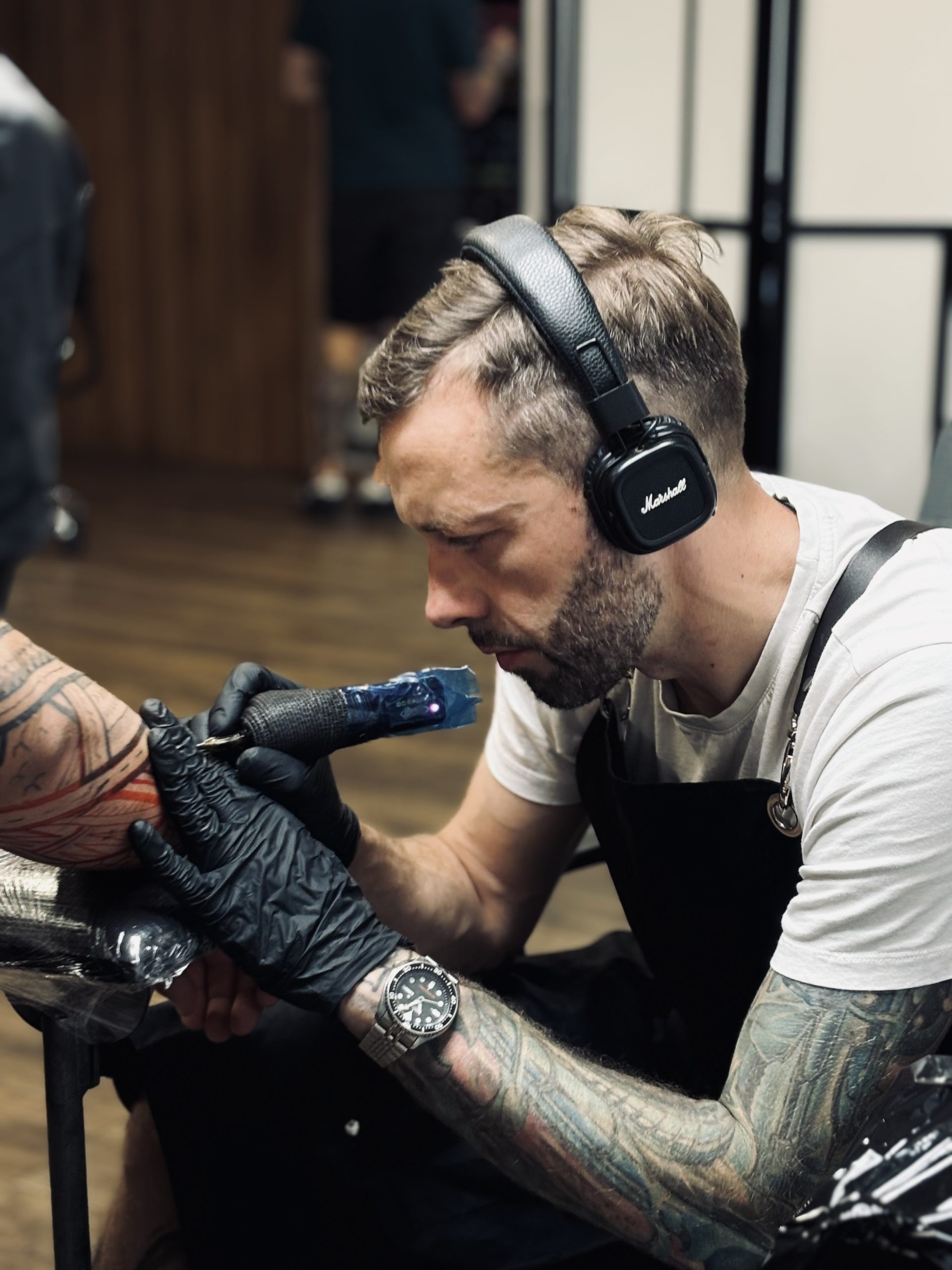 tatuazysta w profesjonalnym studio tatuazu w Poznaniu, wykonywanie tatuażu na ramieniu klienta, usługi tatuatorskie w Poznaniu, nowoczesne studio tatuazu